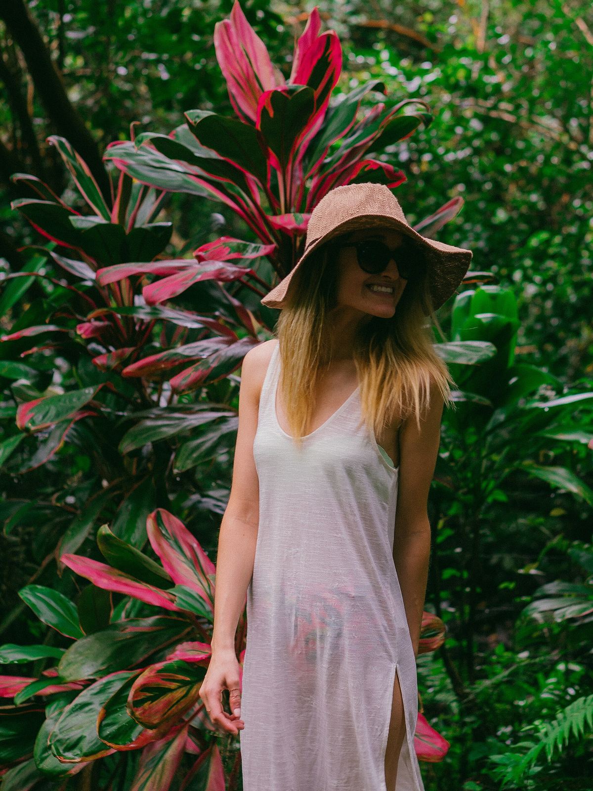 Mulher de vestido slip off-white entre folhagens tropicais